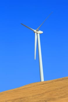 Close up of a wind turbine over blue sky.
