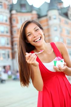 Woman eating ice cream in smiling happy in red summer dress in front of chateau frontenac in Quebec City, Quebec, Canada. Joyful multicultural Asian Caucasian tourist.