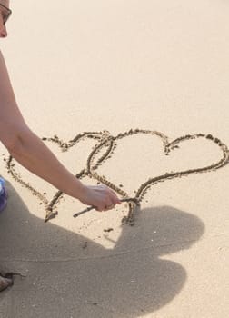 Lady drawing pair of linked hearts in sand on beach in Caribbean