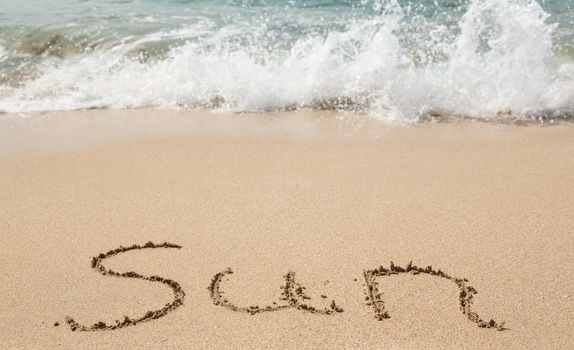 Sand drawing on warm beach by ocean surf in Caribbean spelling Sun