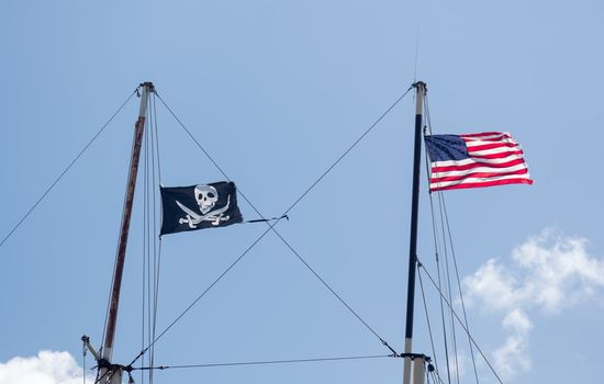 Flags of USA and skull and crossed swords fly from masts of ship