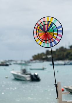 Toy whirligig windmill on dock by harbor with backlit boats in ocean at resort