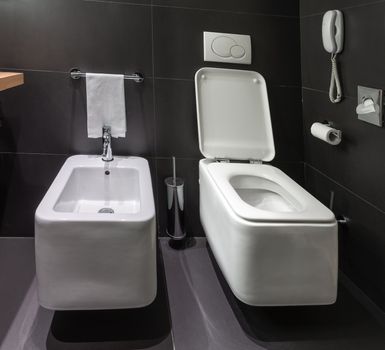 Details of modern square toilet wc and bidet in black tiled bathroom