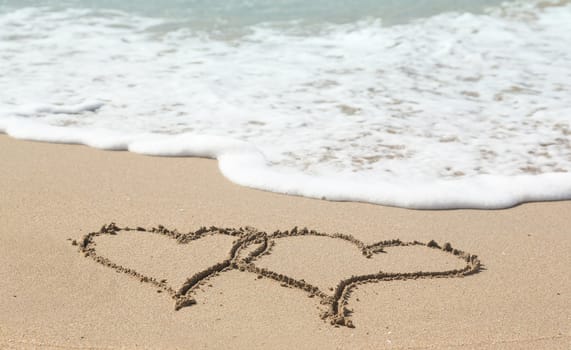 Sand drawing on warm beach by ocean surf in Caribbean with linked hearts