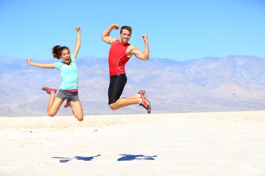 Success - young runners jumping excited celebrating and cheering happy and energetic on dramatic desert landscape. Young joyful sporty fitness interracial fit fitness sport couple, Asian woman, Caucasian man outdoors.