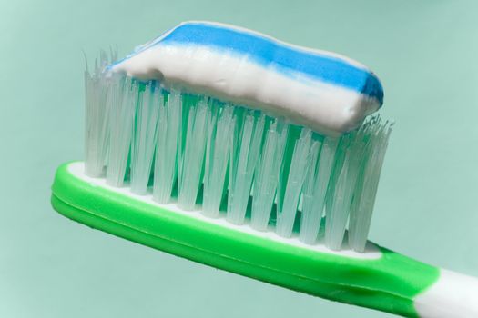 close up view of toothbrush and some toothpaste on it on green back 