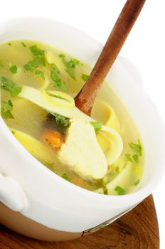 Chicken Noodle Soup with Parsley and Carrot in White Bowl with Wooden Spoon on Wooden Plate closeup on white background