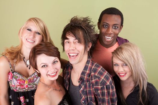 Five urban dressed teens laugh towards the camera in front of a green studio wall.