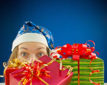 Surprised teen girl looking from behind the Christmas presents