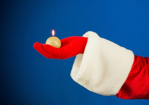 Santa's hand holding a burning candle over blue background