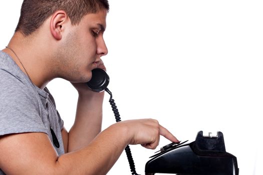 Young man dials a vintage rotary phone isolated over a white background.