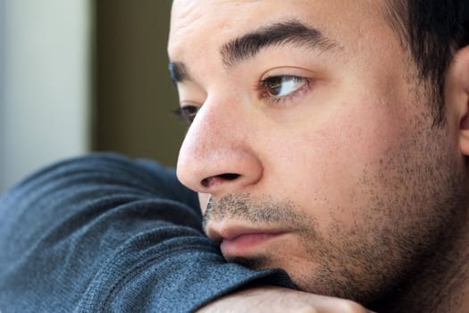 Close up of an unshaven depressed young man gazing off into the distance. Shallow depth of field.