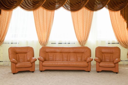 Leather armchairs and a sofa. The interior with curtains