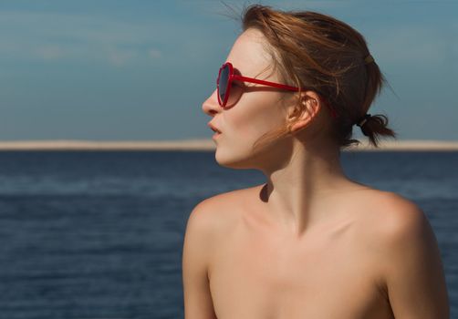 Young red woman wearing sunglasses with sea at background