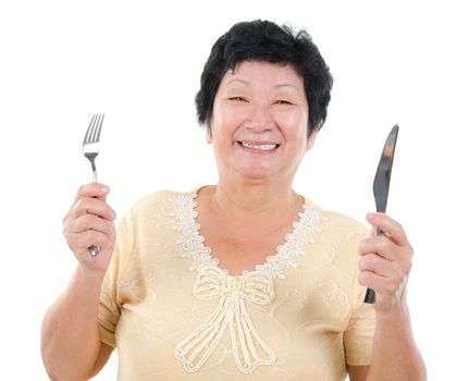 Happy Asian senior mother ready for her Mother's day meal, holding fork and knife isolated on white.