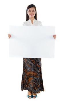 Full body attractive Southeast Asian young woman in traditional batik kebaya costume holding a white blank card standing isolated white background.