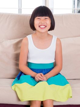 Seven years old Southeast Asian child sitting on sofa at home with happy face