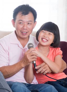 Happy Southeast Asian family living lifestyle. Portrait of a Asian father and daughter singing karaoke through microphone in the living room