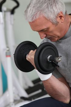 mature white-haired man lifting weight in sports room