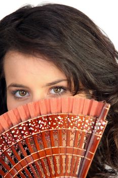 Closeup of a pretty woman hiding behind a fan