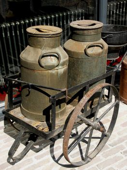 Old wheelbarrow carrying two old milk cans.