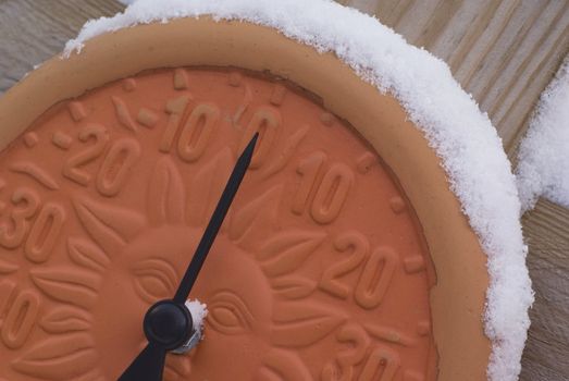 Modern clay thermometer with snow on top of it pointing at 0 degrees Celsius.