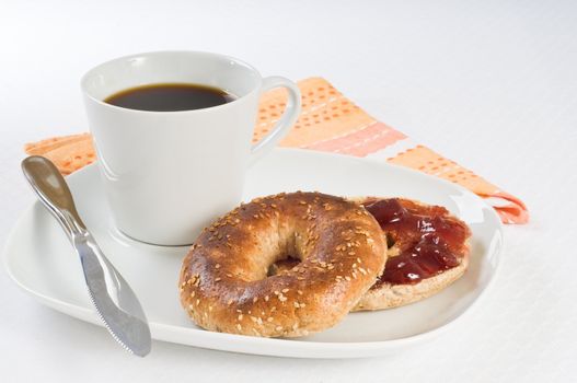 Sesame seed bagel with strawberry jam and coffee.