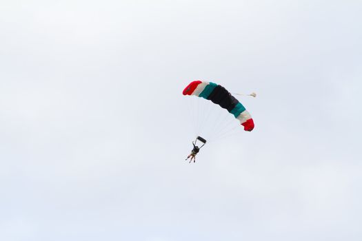 A person skydiving with their parachute open floats towards the ground on the north shore of Oahu. There are clouds in the blue sky with vibrant colors as the skydiver goes in for a landing.