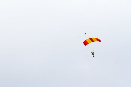 A person skydiving with their parachute open floats towards the ground on the north shore of Oahu. There are clouds in the blue sky with vibrant colors as the skydiver goes in for a landing.