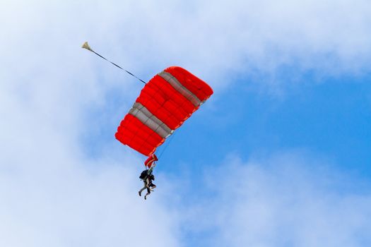 A person skydiving with their parachute open floats towards the ground on the north shore of Oahu. There are clouds in the blue sky with vibrant colors as the skydiver goes in for a landing.