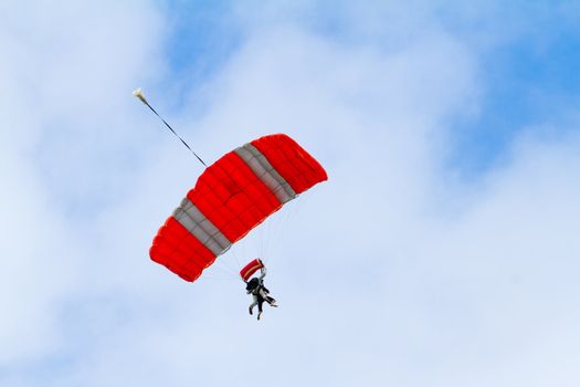 A person skydiving with their parachute open floats towards the ground on the north shore of Oahu. There are clouds in the blue sky with vibrant colors as the skydiver goes in for a landing.