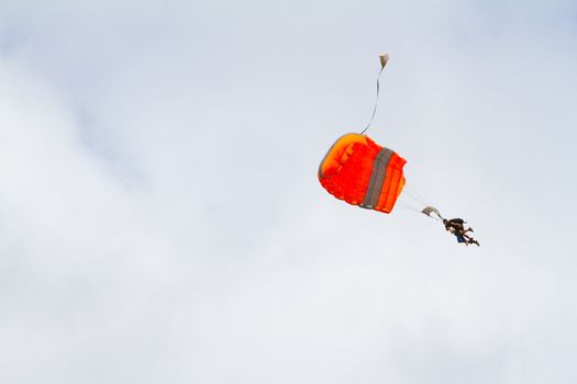 A person skydiving with their parachute open floats towards the ground on the north shore of Oahu. There are clouds in the blue sky with vibrant colors as the skydiver goes in for a landing.