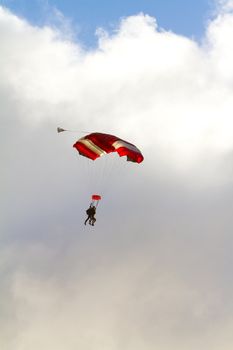 A person skydiving with their parachute open floats towards the ground on the north shore of Oahu. There are clouds in the blue sky with vibrant colors as the skydiver goes in for a landing.