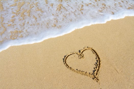 A heart is drawn in the sand on the Hawaii beach showing an image of white sand, water, waves, and the symbol for love. This would be a great image for a honeymoon, valentines day, or any sort of love design that needs a tropical vacation look.
