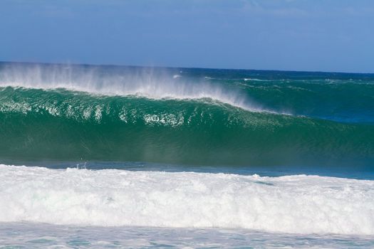 Large waves break off the north shore of oahu hawaii during a great time for surfers surfing. These waves have hollow barrells and are located at pipeline by sunset beach.