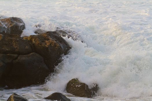 White frothy water rushes in dangerously over some rocks on the north shore of Oahu during a huge storm in the ocean.