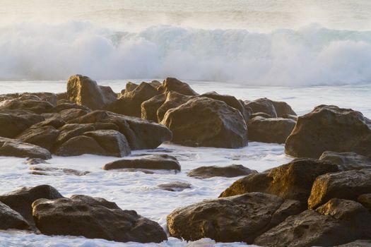 White frothy water rushes in dangerously over some rocks on the north shore of Oahu during a huge storm in the ocean.