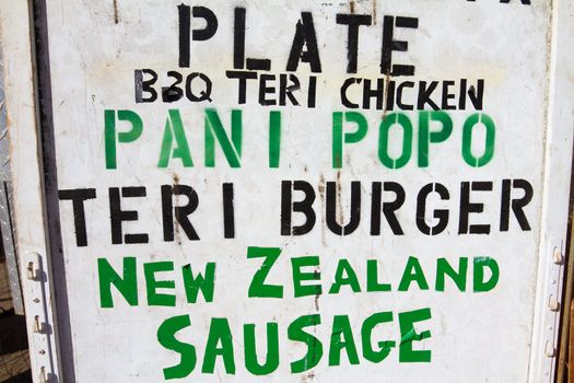 A food truck in Oahu Hawaii has a painted stenciled sign showing the menu for plate lunches.