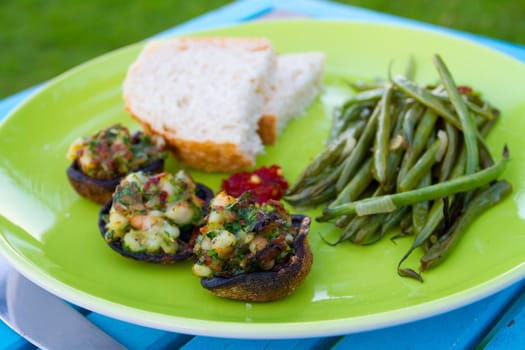 This gourmet meal of stuffed mushrooms and green beans served on a green plate with some white bread. This is dinner but the image applies to lunch also.