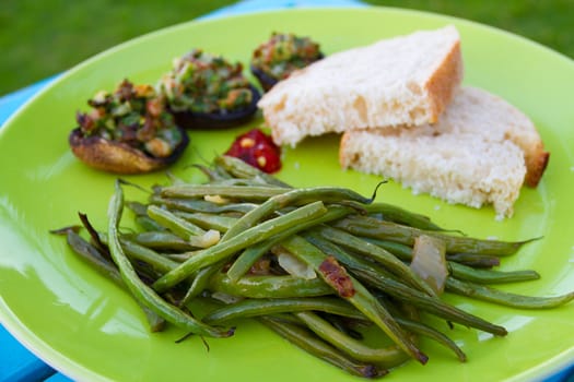 This gourmet meal of stuffed mushrooms and green beans served on a green plate with some white bread. This is dinner but the image applies to lunch also.