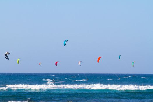 A bunch of people are kite surfing on the north shore of Oahu in Hawaii. This shot shows the man kites in the air with people on surfboards among the ocean waves.