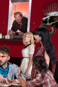 Smiling mulatto woman waiting at mobile pizza cafe next to chef