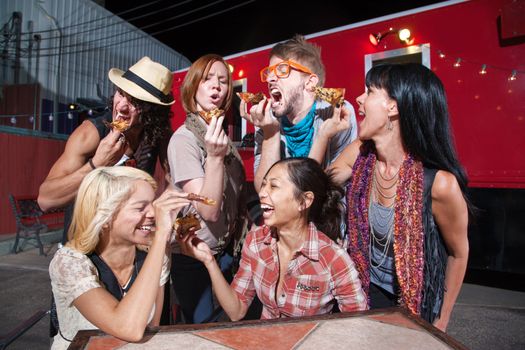 Six laughing people with slices of pizza outdoors