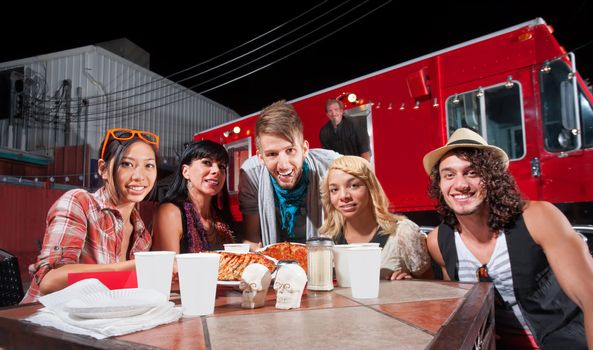 Smiling patrons at table in front of chef and food truck
