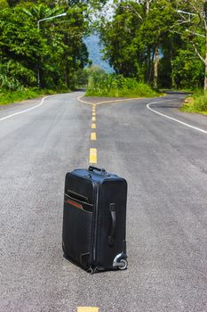 forgotten black suitcase on a country forest road