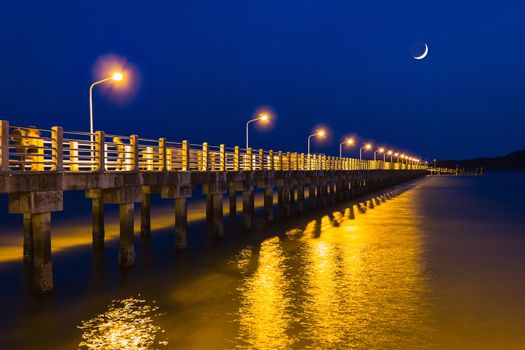 Pier at night with yellow lights on a background of blue sky stretching into the sea