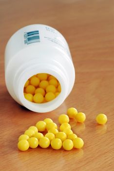 yellow vitamin pills scattered from white plastic bottle