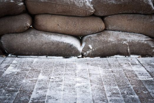 Old brown sandbags on snow covered wooden floor, taken on a winter morning.