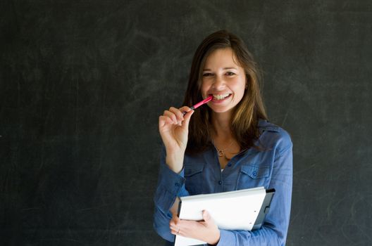 Confident woman with notepad and pen against a blackboard background