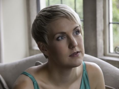 Beautiful blond girl with dreamy look sitting by window.